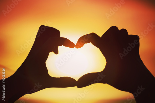 Silhouette of hand in heart shape with sun down