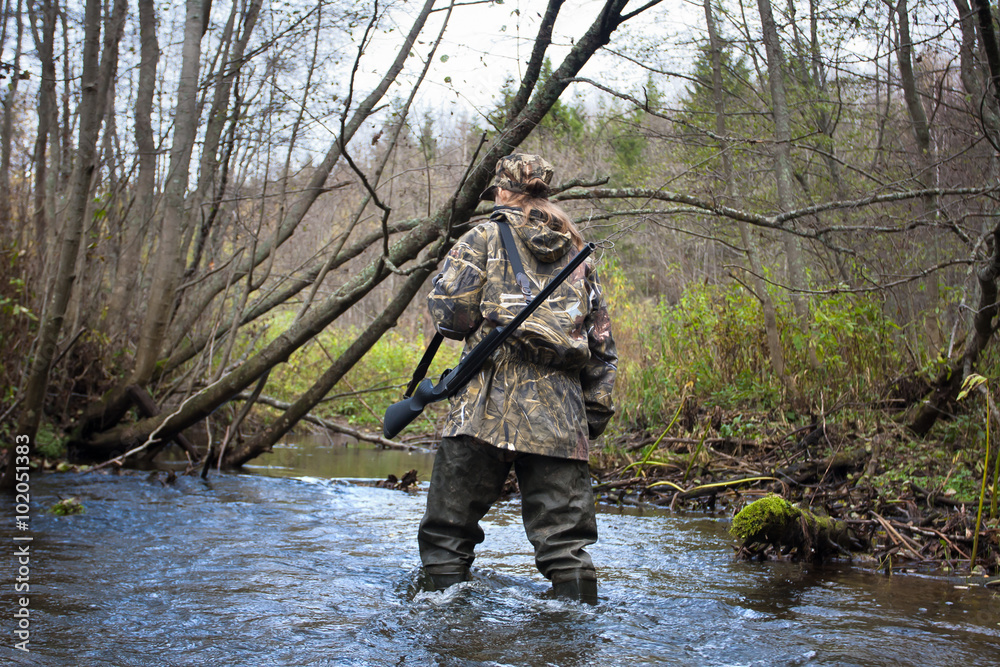 Naklejka premium woman hunter in waders crossing small river in the forest