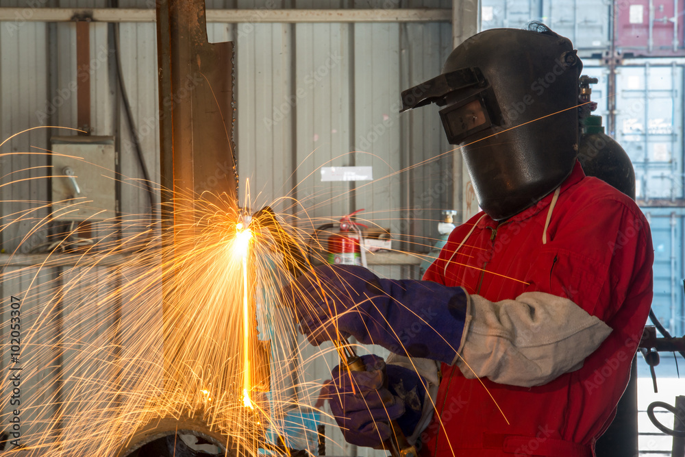 Worker with protective mask welding metal in factory