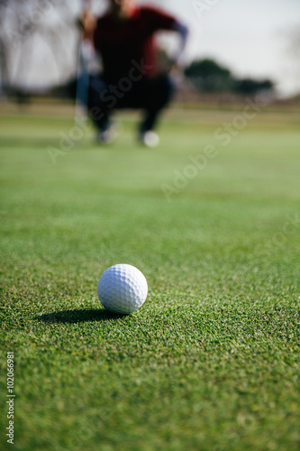 Golf ball with unfocused golfer crouched in the background