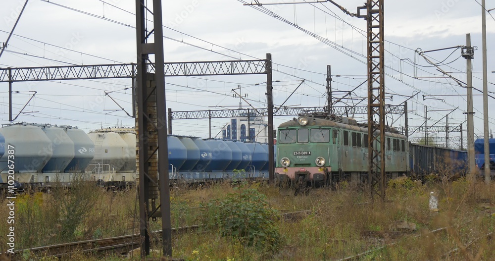 Cargo Train Stands On The Farther Railroad Track Green Electric Locomotive Pulls Long Freight Train Grey And Blue Freight Wagons Cloudy Autumn Day Cargo Train Stands On The Farther Railroad Track Green Electric Locomotive Pulls Long Freight Train Grey And Blue Freight Wagons Cloudy Autumn Day
