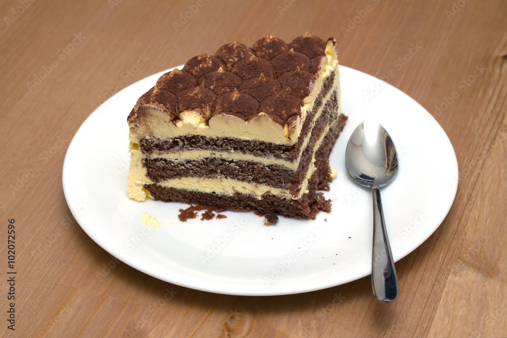 A piece of sponge cake on a white plate with a teaspoon on the wooden table surface. Horizontal photo closeup A piece of sponge cake on a white plate with a teaspoon on the wooden table surface. Horizontal photo closeup