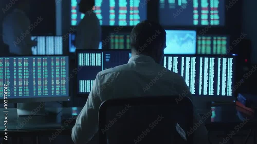 Stockbroker spotted a positive trend in trading charts while working in a dark monitoring room with display screens. Shot on RED Cinema Camera. Stockbroker spotted a positive trend in trading charts while working in a dark monitoring room with display screens. Shot on RED Cinema Camera.