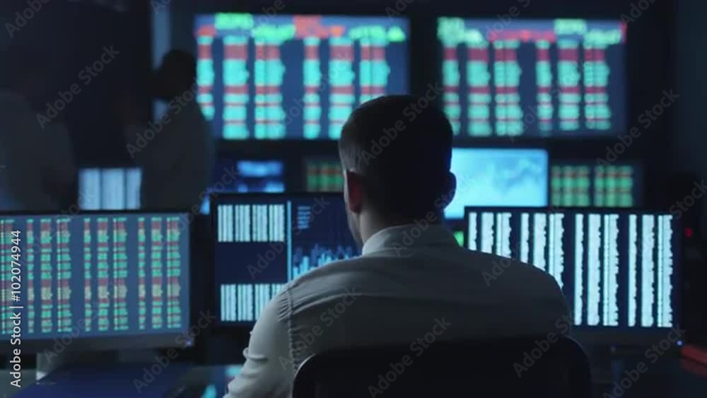 Stockbroker in white shirt is working in a dark monitoring room with display screens. Shot on RED Cinema Camera.