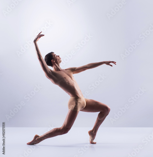 Fototapeta Naklejka Na Ścianę i Meble -  Athletic ballet dancer in a perfect shape performing over the grey background.