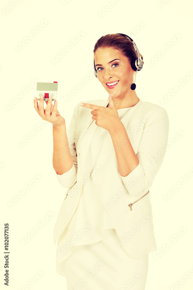 Young businesswoman in headset holds house model