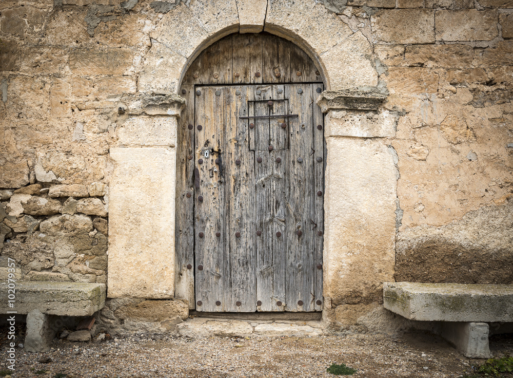 Fototapeta premium ancient wooden door on a stone made wall and cement benches