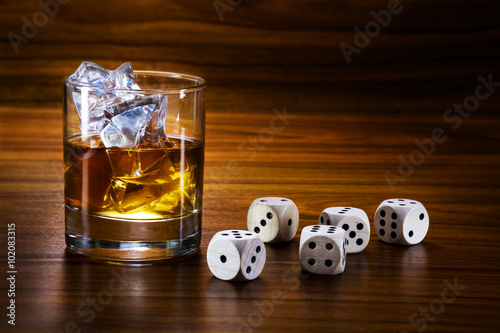 whiskey with ice and dice on a warm toned wooden table, concept photo