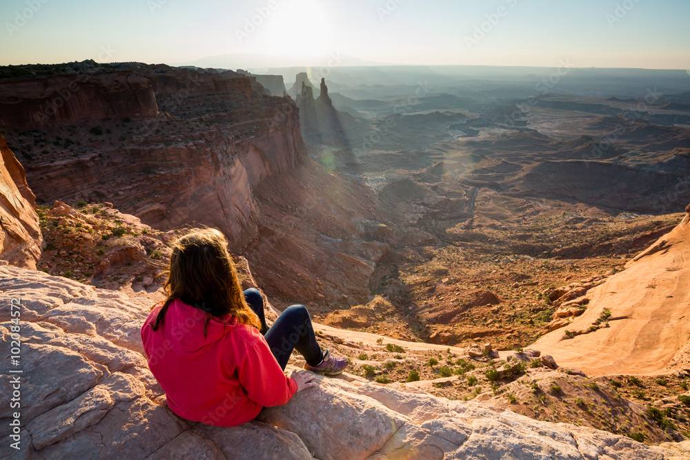 Girl sitting at the Mesa Arch at sunrise, Canyonlands
