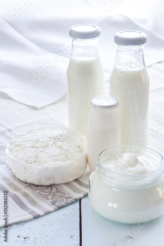 Dairy products. Milk in glass bottle, yogurt, sour milk cheese, sour cream in glass jar, on light blue wooden table