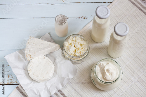 Dairy products. Milk in glass bottle, yogurt, sour milk cheese, sour cream in glass jar, camembert, brie on light blue wooden table