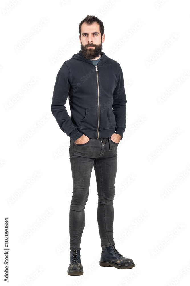 Tough confident stylish punker in black hooded sweatshirt looking at camera with hands in pockets. Full body length portrait isolated over white studio background. Tough confident stylish punker in black hooded sweatshirt looking at camera with hands in pockets. Full body length portrait isolated over white studio background.