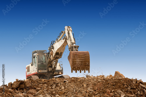 excavator with bucket on gravels blue cloudy sky background