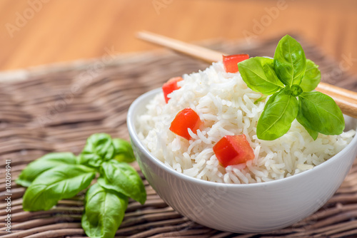 Картината върху платно Cooked basmati rice in a bowl with chipsticks, tomato and basil