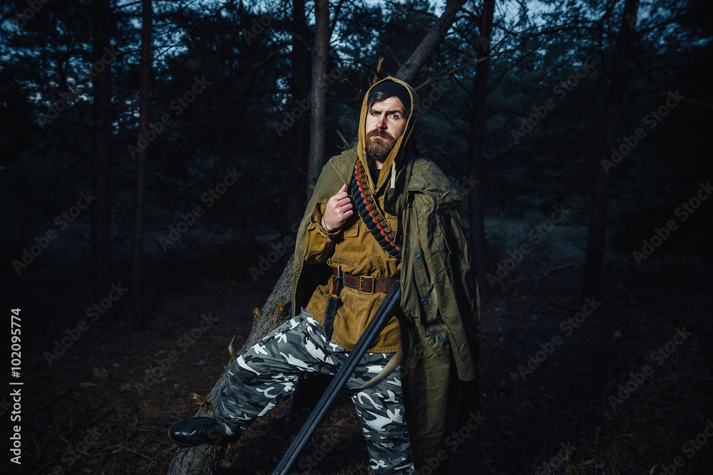 brutal hunter, bearded man in warm hat with a gun in his hand, a knife a backpack and smoking pipe in the dark wild forest in the autumn brutal hunter, bearded man in warm hat with a gun in his hand, a knife a backpack and smoking pipe in the dark wild forest in the autumn