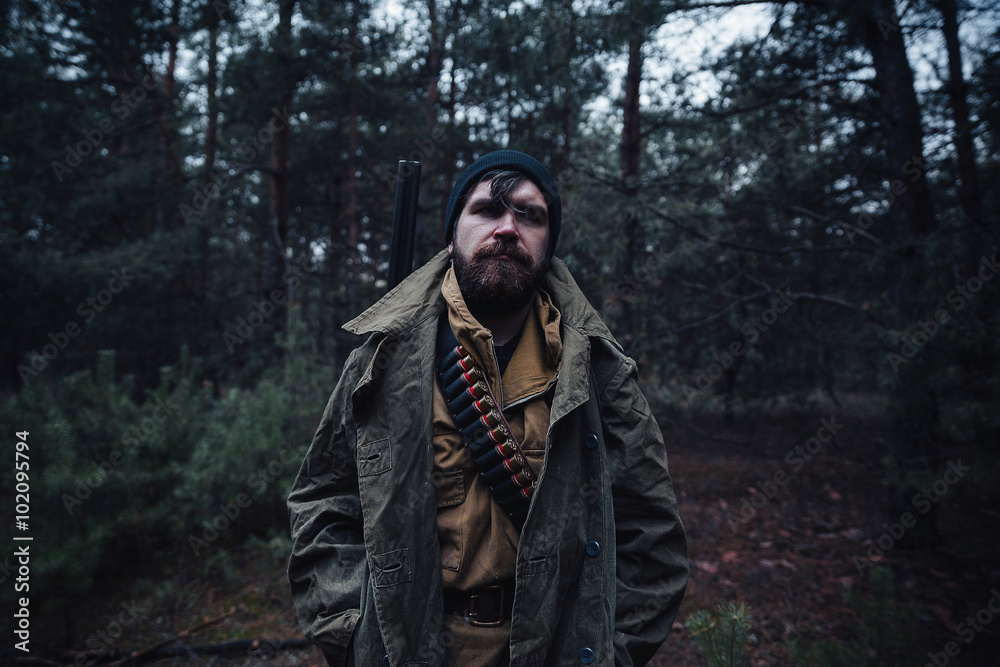 brutal hunter, bearded man in warm hat with a gun in his hand, a knife a backpack and smoking pipe in the dark wild forest in the autumn brutal hunter, bearded man in warm hat with a gun in his hand, a knife a backpack and smoking pipe in the dark wild forest in the autumn