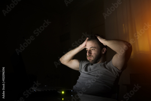 Chico joven trabajando en su casa se lleva las manos a la cabeza frente a su ordenador photo
