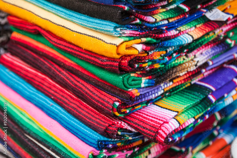 Colorful Mexican serapes hang in row. 