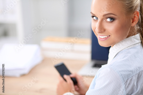 Businesswoman sending message with smartphone sitting in the office