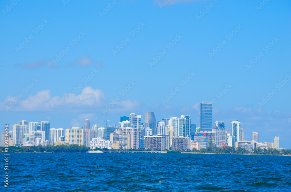 Colorful photo of the Miami skyline as viewed off of the coastline in Biscayne Bay, Florida on a blue sky sunny morning.