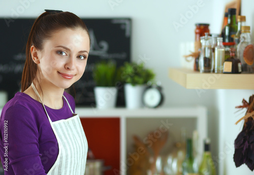 Young woman standing in her kitchen near desk with shopping bags
