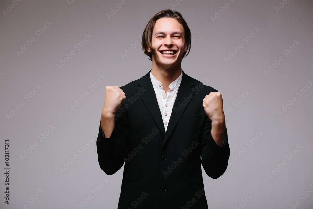 Business world. View of excited young businessman keeping arms raised and expressing positivity while standing against white background Business world. View of excited young businessman keeping arms raised and expressing positivity while standing against white background