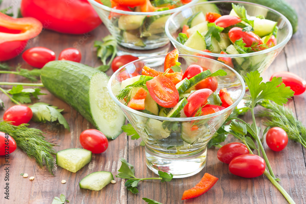 Three glass bowls with a salad of fresh vegetables and ingredients - tomato, cucumber, bell pepper on a dark wooden background

