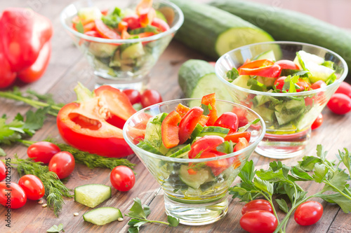 Three glass bowls with a salad of fresh vegetables and ingredients - tomato, cucumber, bell pepper on a dark wooden background
