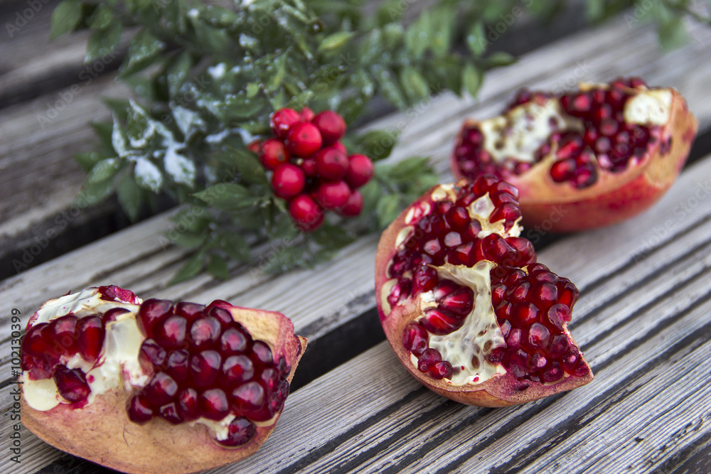 Juicy pomegranate fruit and red flower over wooden table Juicy pomegranate fruit and red flower over wooden table