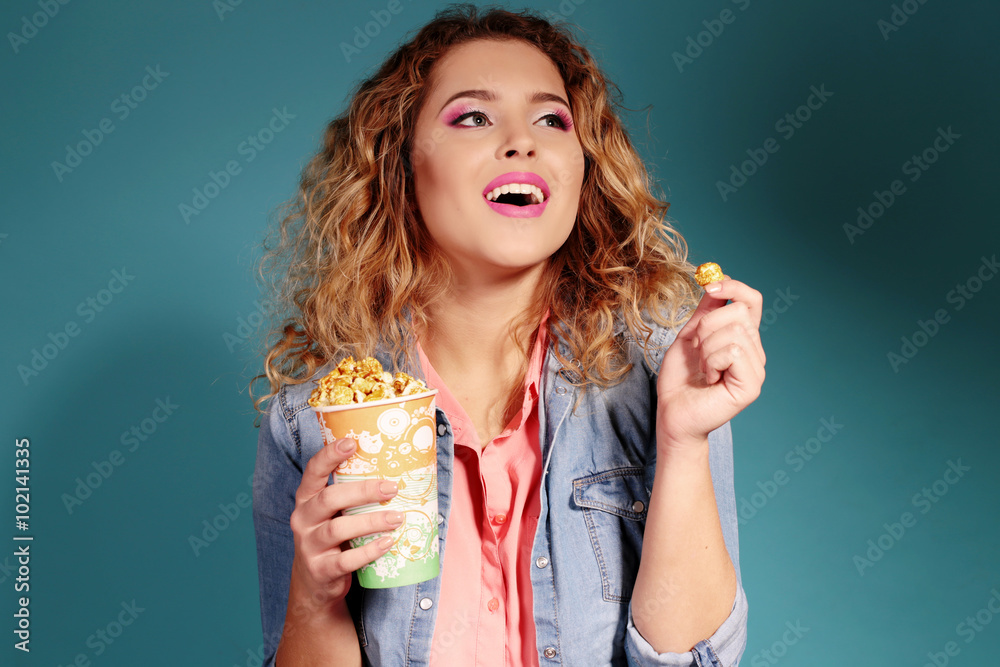 fashion studio photo of beautiful young woman with blond curly hair wears casual clothes, eating popcorn