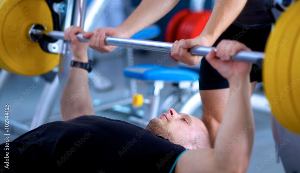 Fototapeta premium Young man lifting the barbell in gym with instructor