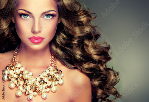 Beautiful model brunette with long curled hair . Girl with big necklace with beads and chain . Jewelry and accessories .Hairstyle wavy curls . Makeup color fuchsia . 