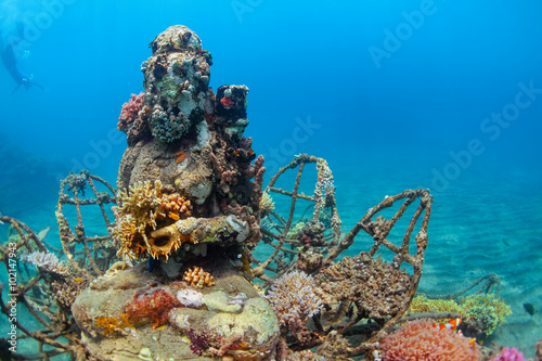 Buddha statue on sea sand bottom on background of snorkeler swimming deep down into water to observe tropical reef. Vacation adventures and underwater safari on scuba diving sites in Bali, Indonesia. photo