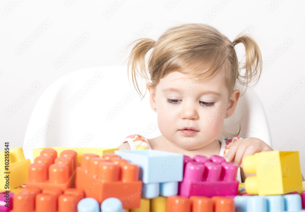 Adorable little girl sitting on chair and playing with colorful toy blocks Adorable little girl sitting on chair and playing with colorful toy blocks