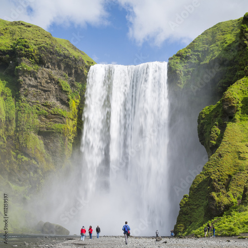 walking people under big waterfall in Iceland