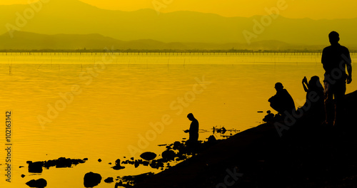 Silhouette of men stand beside the lake © Khwanchai