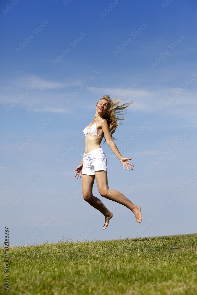 The happy woman in white bikini and shorts jumps in a summer green field The happy woman in white bikini and shorts jumps in a summer green field