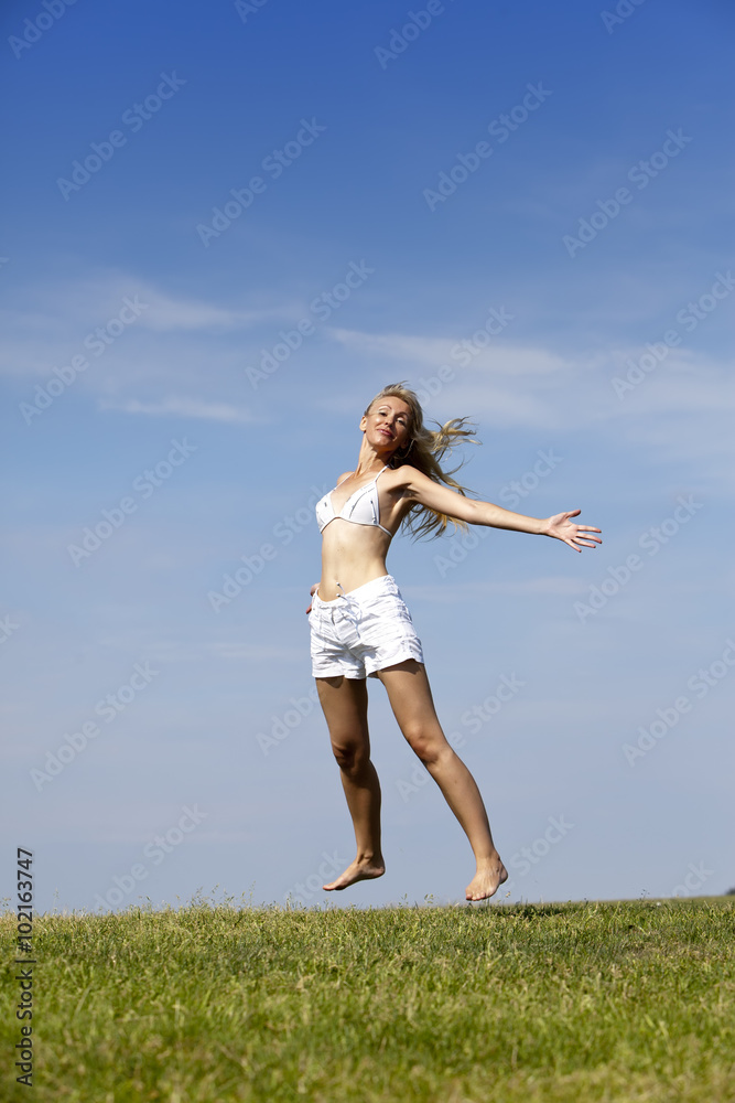 The happy woman in white bikini and shorts jumps in a summer green field The happy woman in white bikini and shorts jumps in a summer green field