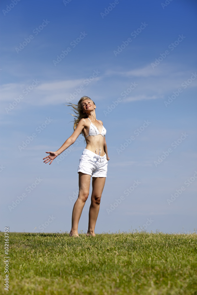 The happy woman in white bikini and shorts in a summer green field The happy woman in white bikini and shorts in a summer green field