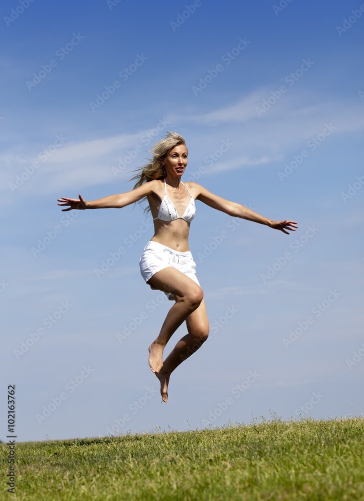 The happy woman in white bikini and shorts jumps in a summer green field The happy woman in white bikini and shorts jumps in a summer green field