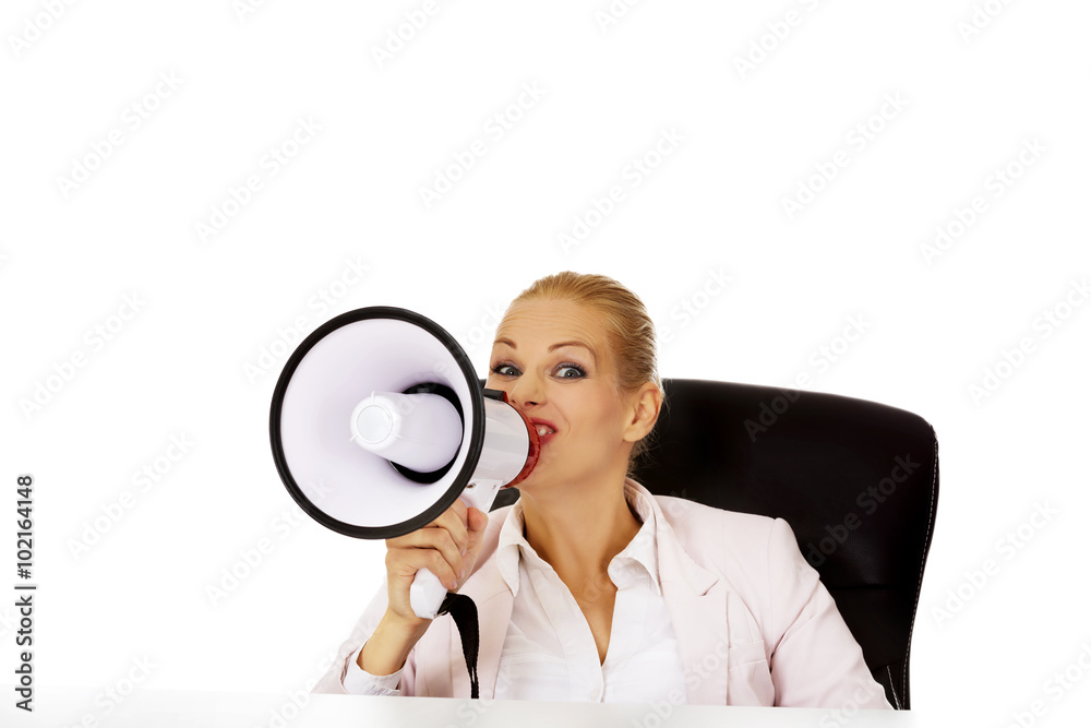 Business woman sitting behind the desk and screaming through a megaphone Business woman sitting behind the desk and screaming through a megaphone