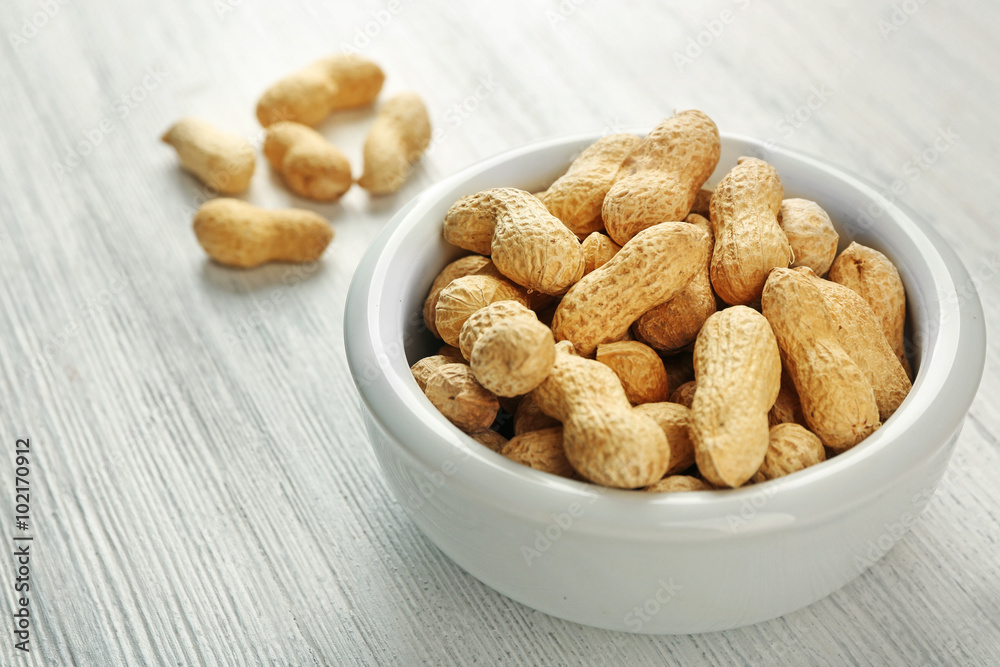 Peanuts in the bowl on white wooden background Peanuts in the bowl on white wooden background