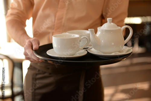 Waiter holding tray with teapot and cups close up