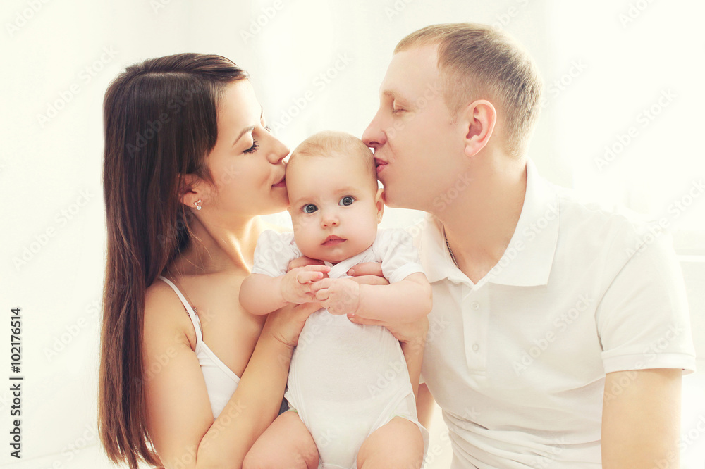 Happy family, mother and father kissing baby in white room Happy family, mother and father kissing baby in white room