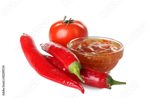 hot sauce in a bowl. Nearby is pure tomatoes with pepper isolated on white background