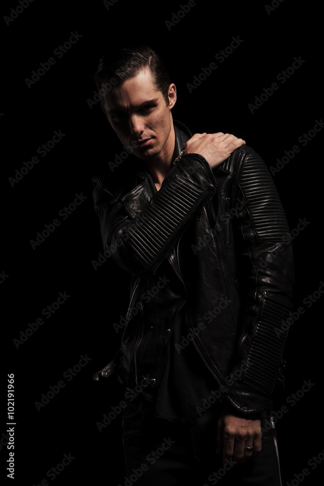 Fototapeta premium confident rocker in black leather jacket posing in dark studio