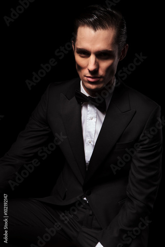 confident model in black suit posing seated in dark