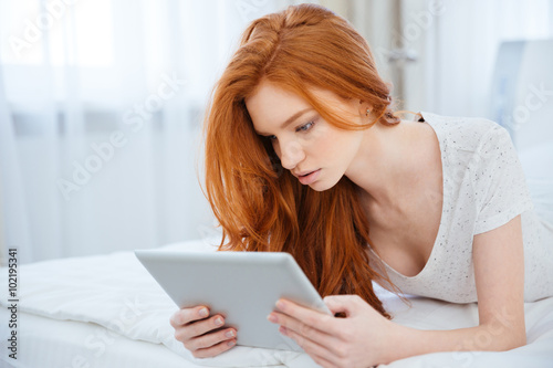 Redhead woman using tablet computer on the bed