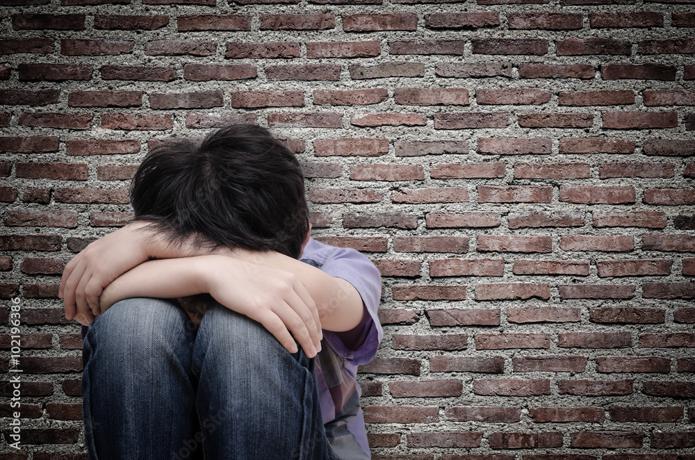 Little sad boy sitting on floor over old wall