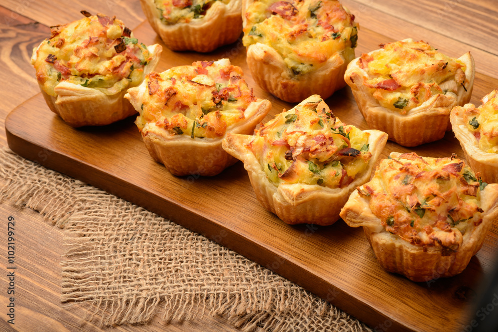Tartlets baked with mashed potato, cheese, ham and parsley, on wooden background.